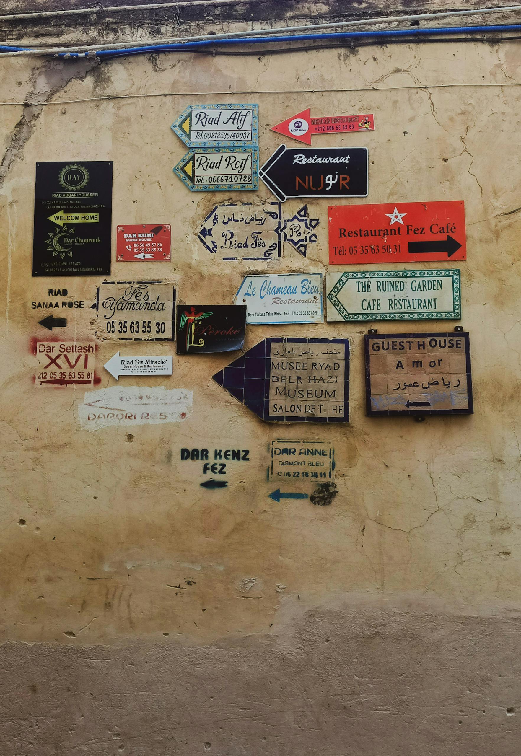Various colorful signs on a wall in Fès, Morocco, showcasing local business directions.